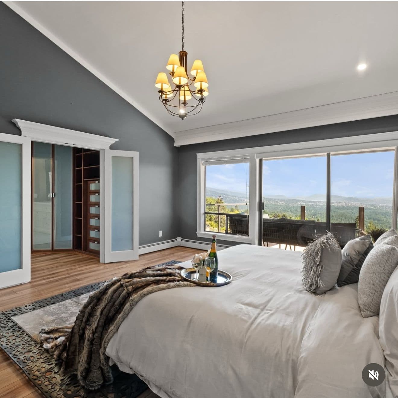 Staged primary bedroom in soft grey with mountain views and a faux-fur throw